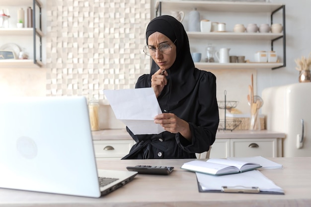 Mulher árabe em casa fazendo papelada mulher muçulmana concentrada em hijab segurando contas nas mãos