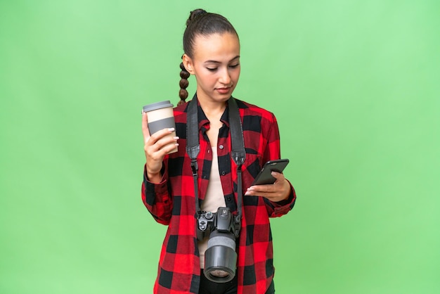 Mulher árabe jovem fotógrafo sobre fundo isolado segurando café para levar e um celular