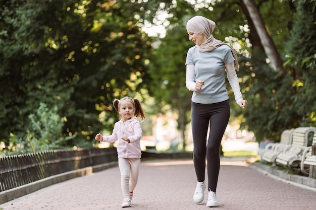 Mulher árabe muçulmana gostando de correr juntas no parque com sua linda filha ativa de 4 anos