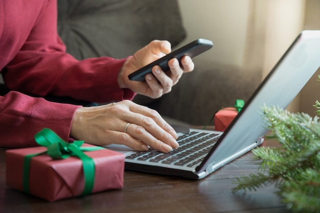 Mulher às compras com smartphone pelo laptop no interior de casa.