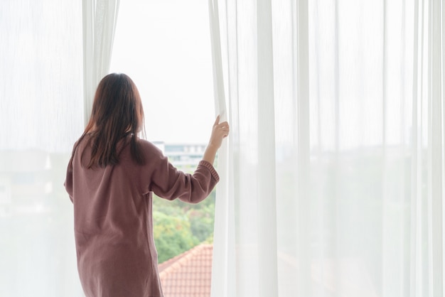 Mulher asiática abre a cortina de manhã