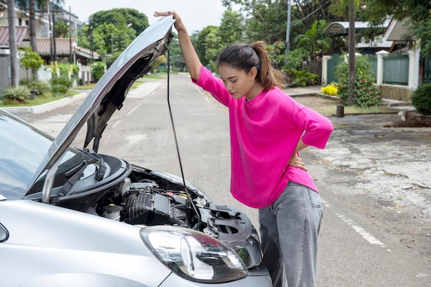 Foto mulher asiática abrindo o capô do carro e procurando problemas, o carro quebra