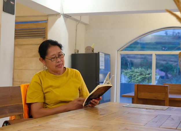 Mulher asiática adulta a passar o tempo livre a ler romances na sala de jantar.