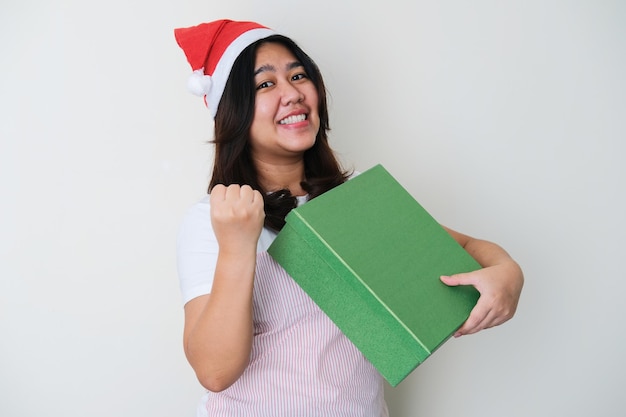 Mulher asiática adulta usando chapéu de Natal e mostrando uma expressão de felicidade enquanto segura uma caixa de pacote de presente