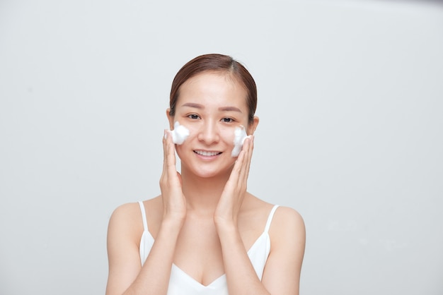 Mulher asiática alegre aplicando limpador de espuma, tem uma pele limpa, fresca e saudável.