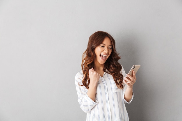 Mulher asiática alegre isolada, segurando um telefone celular, comemorando