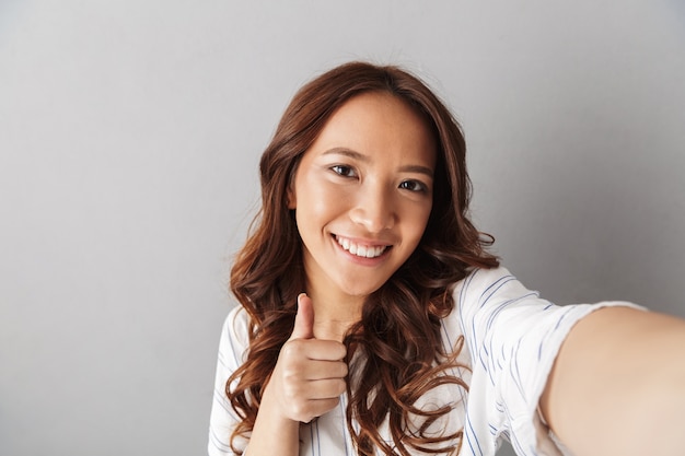 Mulher asiática alegre parada isolada, tirando uma selfie