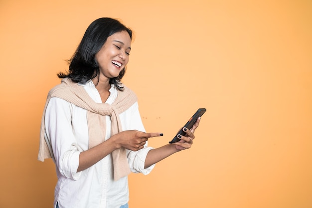 Mulher asiática animada ri com o dedo apontando em seu celular