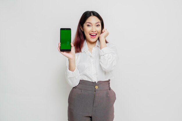 Mulher asiática animada vestindo camisa branca apontando para o espaço da cópia ao lado dela enquanto segura o telefone isolado pelo fundo branco