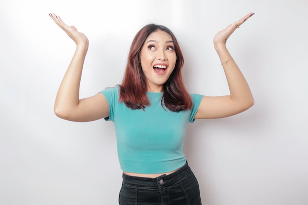 Mulher asiática animada vestindo camiseta azul apontando para o espaço de cópia em cima dela isolada por fundo branco