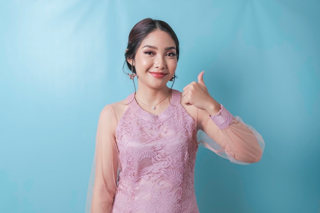 Mulher asiática animada vestindo roupas modernas de kebaya dando polegares para cima gesto com a mão