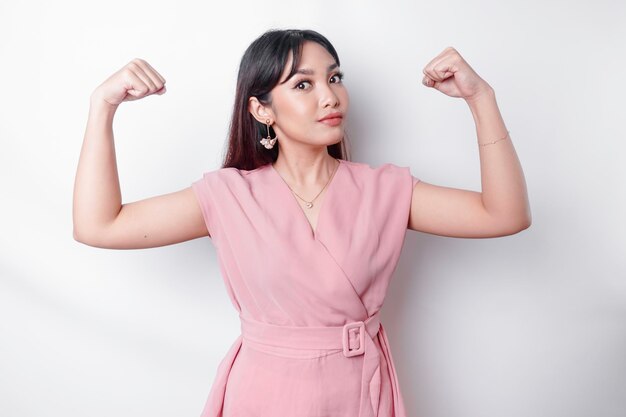 Mulher asiática animada vestindo uma blusa rosa mostrando um gesto forte levantando os braços e os músculos sorrindo com orgulho