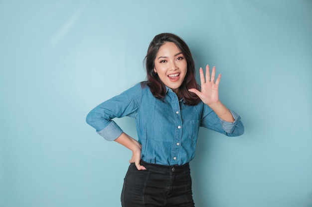 Mulher asiática animada vestindo uma camisa azul dando o número 12345 por gesto de mão