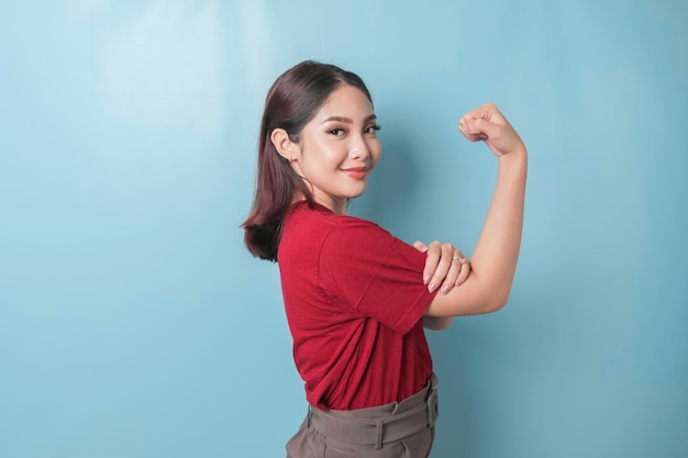 Mulher asiática animada vestindo uma camiseta vermelha mostrando um gesto forte levantando seus braços e músculos sorrindo orgulhosamente