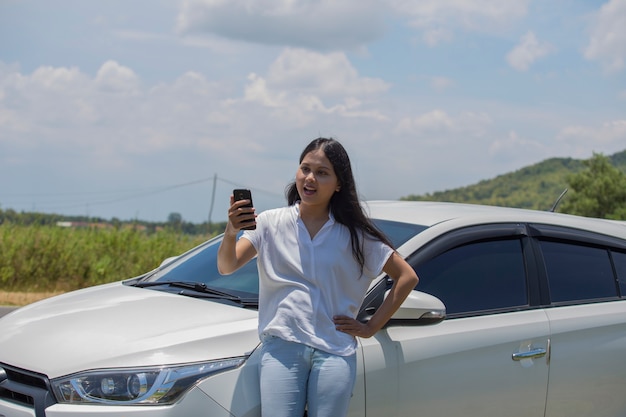 Mulher asiática ao lado de um carro usando um smartphone