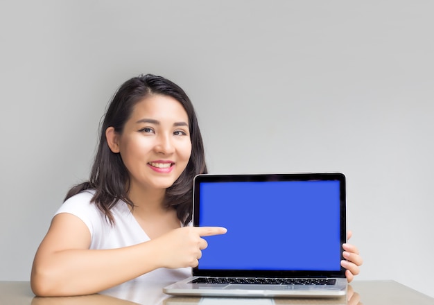 mulher asiática aponta para tela em branco do laptop para exibir