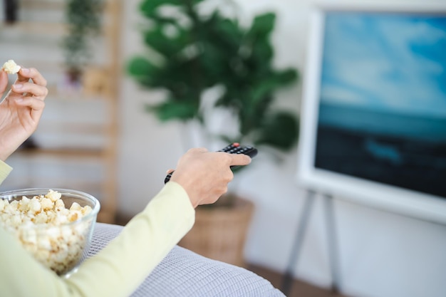 Mulher asiática Assistindo TV inteligente e usando o controle remoto Mão segurando o controle remoto de áudio da televisão em casa com a televisão de controle remoto