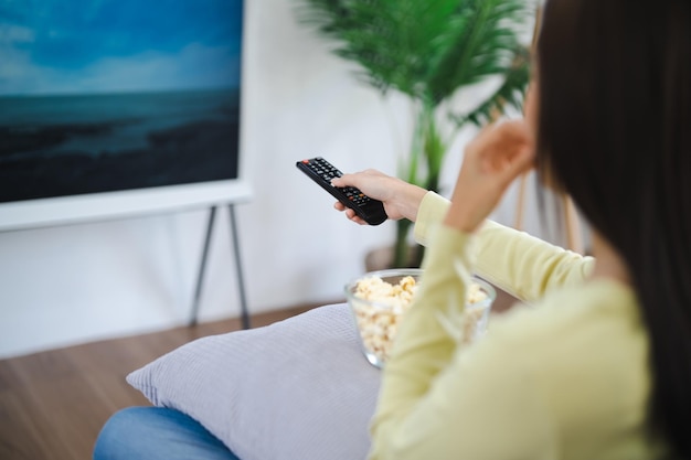 Mulher asiática Assistindo TV inteligente e usando o controle remoto Mão segurando o controle remoto de áudio da televisão