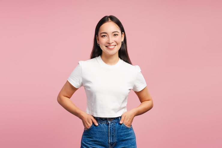 Foto mulher asiática atraente e sorridente com as mãos nos bolsos posando isolada em fundo rosa