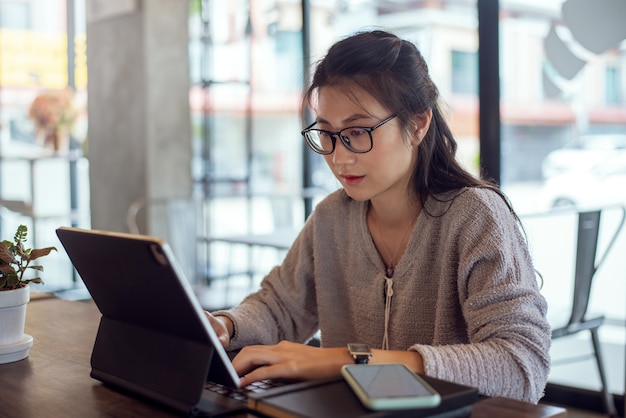 Mulher asiática atraente trabalhando com um tablet digital em uma cafeteria.