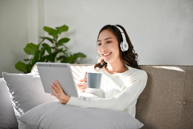 Mulher asiática atraente usando fones de ouvido gosta de assistir filme em seu tablet