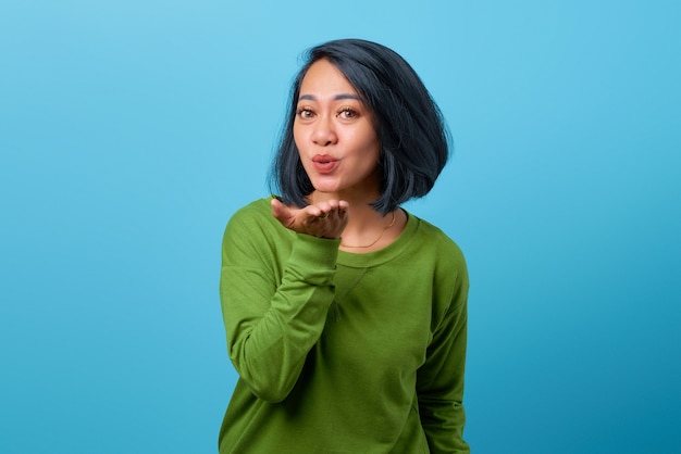 Mulher asiática atraente usando roupas casuais mandando beijo no ar sobre fundo azul