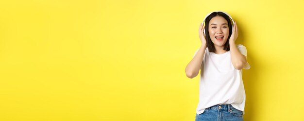 Mulher asiática atrativa que gosta de ouvir música em fones de ouvido sem fio sorrindo satisfeita e cantando um