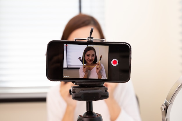 Foto mulher asiática beleza vlogger ou blogger transmissão ao vivo do clipe de tutorial de maquiagem cosmética por telefone celular e compartilhamento no canal de mídia social ou site, estilo de vida do influenciador e selfies tirando fotos