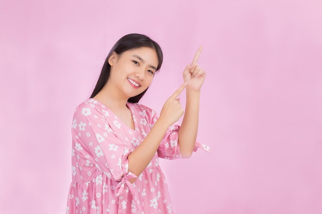 Mulher asiática bonita com cabelo comprido preto em uma camisa rosa mostra a mão apontando para cima para apresentar algo