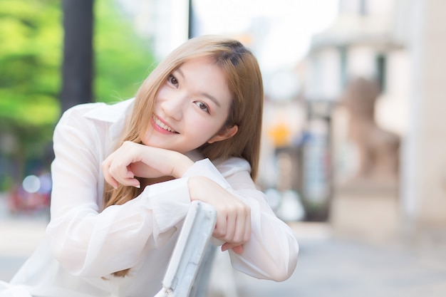 Mulher asiática bonita com cabelo cor de bronze em uma camisa branca enquanto se senta com um sorriso feliz