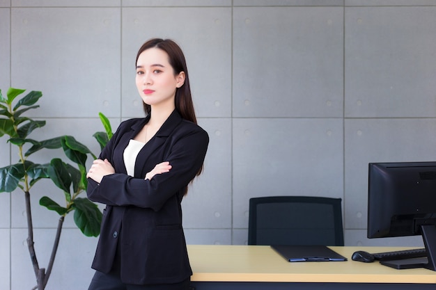 Mulher asiática bonita de negócios bem-sucedida que tem cabelo comprido e usa um terno formal preto com camisa azul
