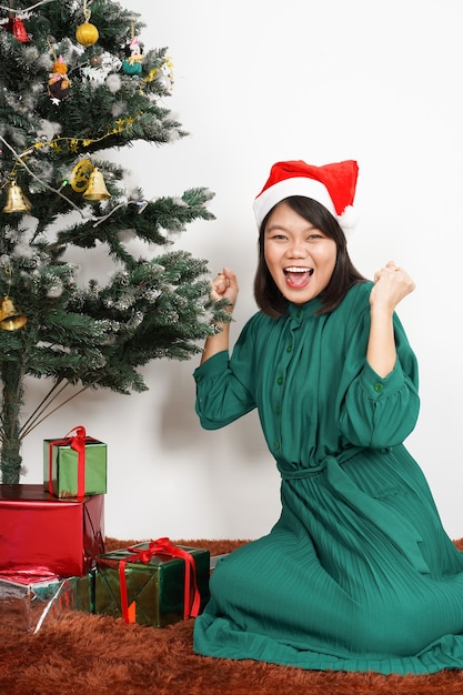 Mulher asiática bonita e feliz usando vestido verde e chapéu de Papai Noel. Comemoração de Natal segurando um presente