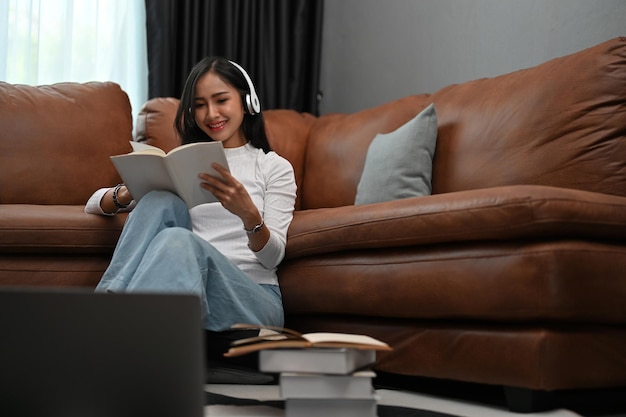 Mulher asiática bonita e relaxada gosta de ler seu livro favorito enquanto ouve música