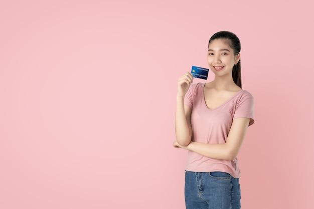 Mulher asiática bonita que guarda o pagamento com cartão de crédito no fundo cor-de-rosa com espaço da cópia.
