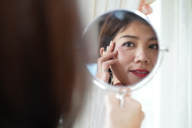 Mulher asiática bonita que olha o espelho para verificar suas rugas