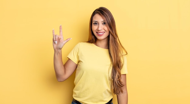 Mulher asiática bonita se sentindo feliz, divertida, confiante, positiva e rebelde, fazendo sinal de rock ou heavy metal com a mão