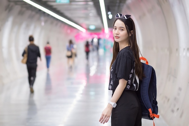 Mulher asiática bonita usando uma camisa preta, ela entra no túnel do metrô e segura uma mochila