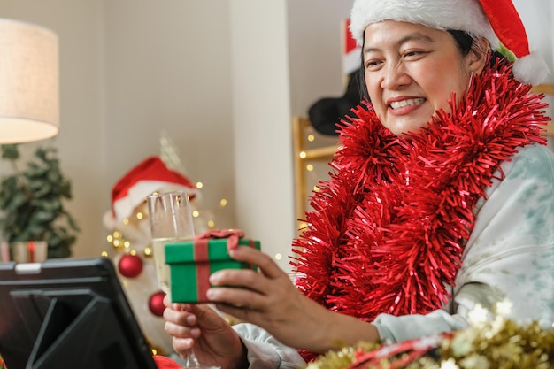 Mulher asiática brindando com champanhe para comemorar o ano novo e a festa de Natal com videochamada para amigos em casa