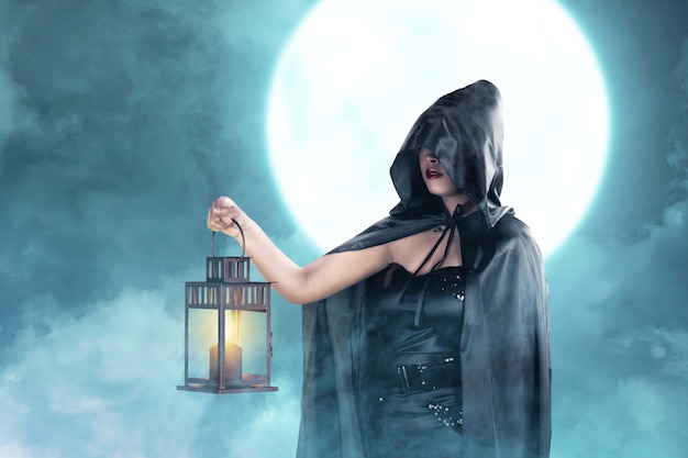 Mulher asiática bruxa com capa preta segurando lanterna em pé
