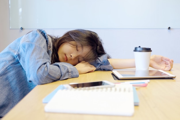 Mulher asiática cansado que dorme na mesa de escritório.