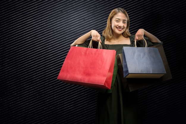 Mulher asiática carregando uma sacola de compras com um fundo preto. Conceito de Black Friday