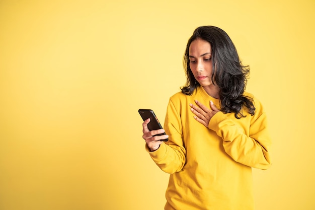 Mulher asiática chocada ao olhar para seu celular em fundo isolado