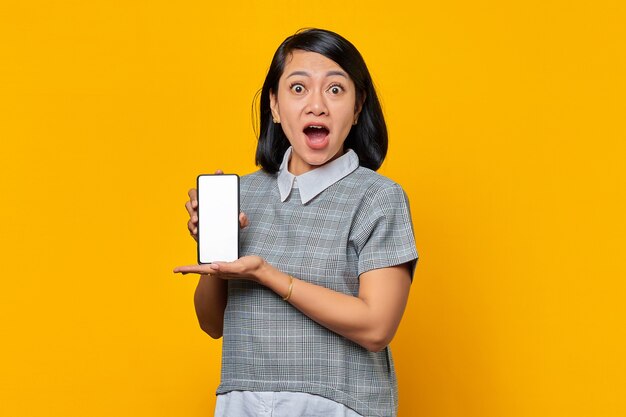 Mulher asiática chocada mostrando a tela em branco do smartphone com a palma da mão. conceito de promoção de produto