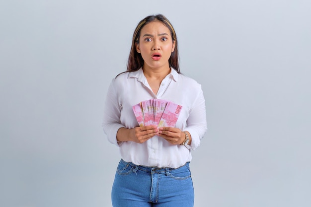 Mulher asiática chocada segurando notas de dinheiro isoladas sobre fundo branco