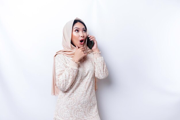 Mulher asiática chocada usando hijab segurando seu telefone isolado por fundo branco