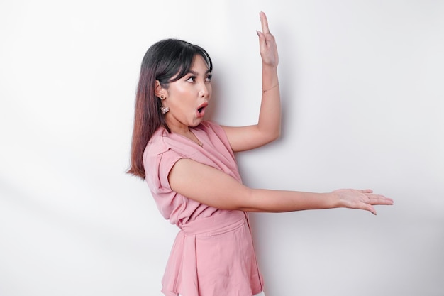 Foto mulher asiática chocada vestida de rosa apontando para o espaço da cópia ao lado dela isolado por fundo branco