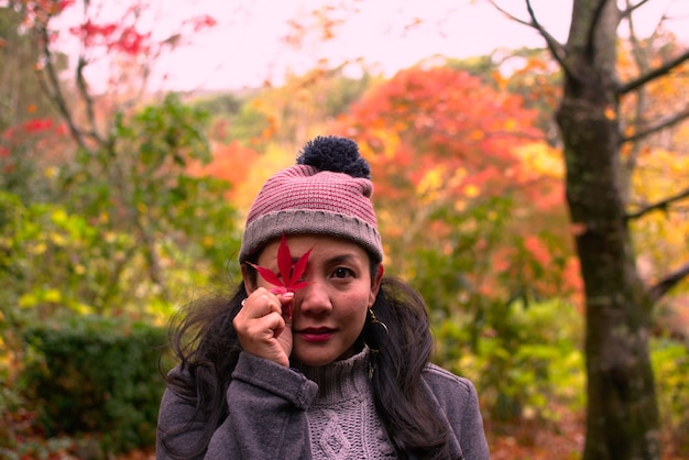 Foto mulher asiática colocar a licença de maple em seu olho direito em pé no outono folhas no ba