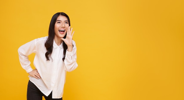 Mulher asiática com a boca aberta levantando as mãos gritando anúncio no fundo do espaço da cópia amarela