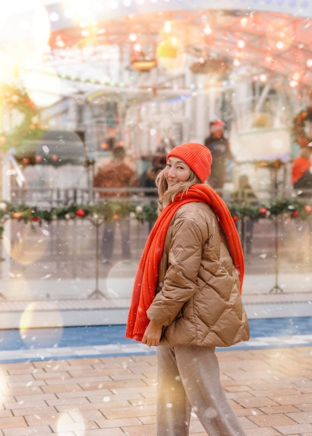 Mulher asiática com cachecol laranja e chapéu andando no mercado de Natal decorado Sentindo-se feliz na cidade