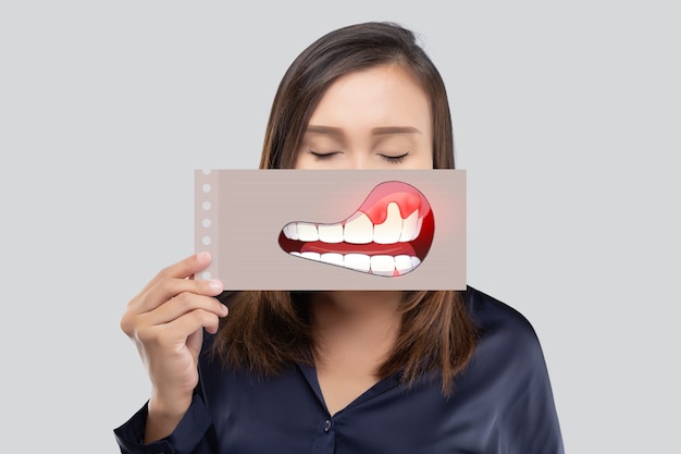 Mulher asiática com camisa azul escura segurando um papel com a imagem de periodontal e gengivite de sua boca contra o fundo cinza